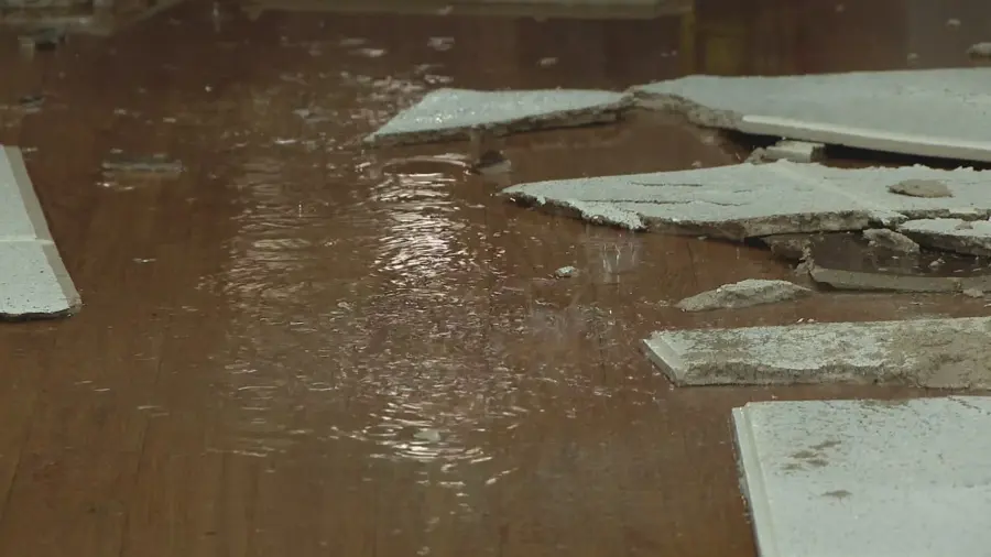 Water across a wood floor with fallen ceiling panels after a pipe leak above