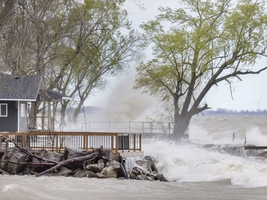 Storm waves breaking over a shoreline deck beside lakefront homes, the kind of surge the Monroe shore sees
