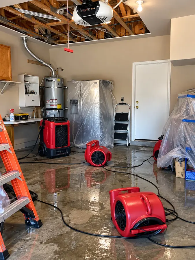 Oregon water damage restoration: air movers and plastic containment drying a wet garage floor around a water heater