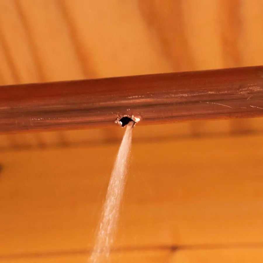 Monroe burst pipe water damage: a copper supply pipe spraying from a pinhole split