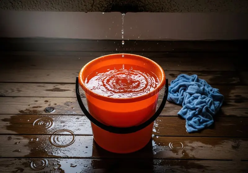 Monroe roof leak water damage: a bucket catching water dripping onto a wood floor
