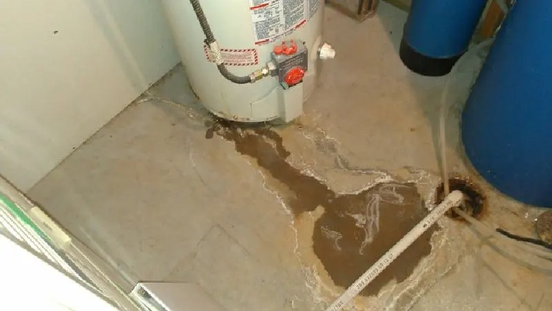 Monroe water heater leak cleanup: a leaking tank spreading rusty water across a basement floor